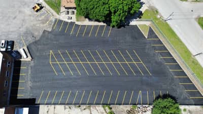 Aerial view of a newly paved asphalt parking lot beside a brick commercial building